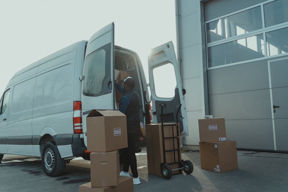 A man standing beside an open white moving van on a residential street during daylight, engaged in a home relocation process as part of furniture transport and packing and moving activities. The man,